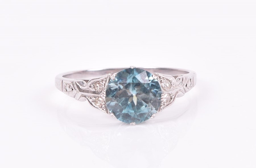 A 9ct white gold, blue zircon, and diamond ring set with a round-cut natural zircon, the shoulders