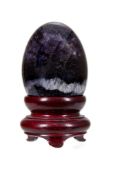 A Blue John egg ornament, the polished Blue John of ovoid form, sitting in a wooden stand, egg