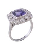 A tanzanite and diamond ring, the central cushion shaped tanzanite collet set within a surround of