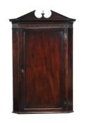 A George III mahogany hanging corner cupboard, circa 1760, the arched pediment above a blind fret