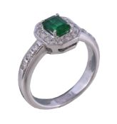 An emerald and diamond ring, the rectangular cut emerald, in a four claw setting, within a surround