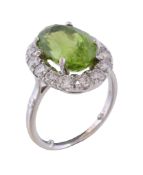 A peridot and diamond cluster ring, the oval cut peridot claw set within a surround of brilliant