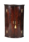 A George II mahogany bowfront hanging corner cupboard, circa 1750, the bookmatched doors enclosing
