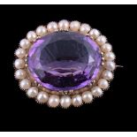 An Edwardian amethyst and half pearl brooch, the oval cut amethyst in a collet setting, within a