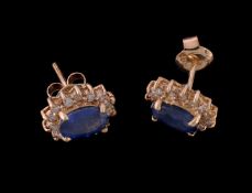 A pair of sapphire and diamond cluster ear studs, the oval cut sapphires within a surround of