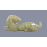 A Chinese yellow jade carving of a hound, recumbent with head turned back, with some natural