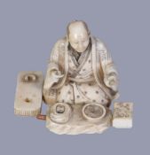 Y A Japanese Ivory Figure of a kneeling scholar surrounded by his inkstone and other