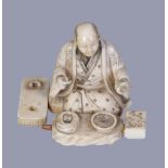 Y A Japanese Ivory Figure of a kneeling scholar surrounded by his inkstone and other