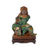 A Chinese glazed Pottery Figure of Guan Yu, seated on a hollowed base with his legs apart and one