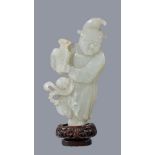 A Chinese celadon jade figure of a ‘Foreigner’, standing holding a vase, the jade 13cm high, glued