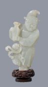 A Chinese celadon jade figure of a ‘Foreigner’, standing holding a vase, the jade 13cm high, glued