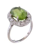 A peridot and diamond cluster ring, the oval cut peridot claw set within a surround of brilliant cut