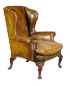A pair of walnut and studded green leather upholstered wing armchairs, in George II style, late
