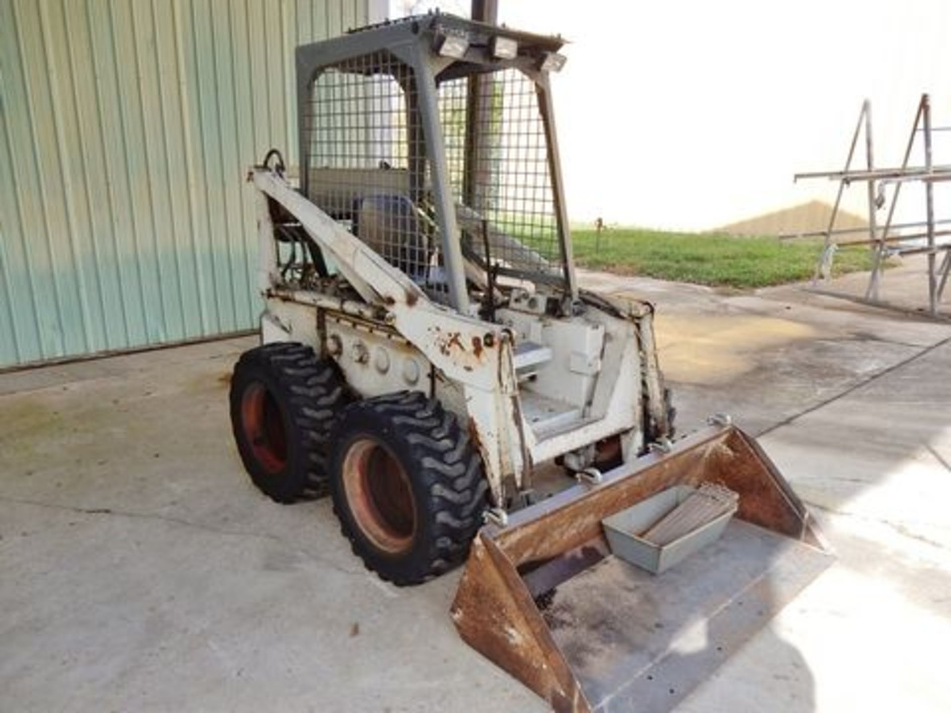 PROCEED OUTSIDE: MELROE/BOBCAT SKID STEER, M# 610, RUBBER TIRES, 60" BUCKET, GAS, OPEN CAB