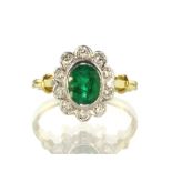 An emerald and diamond cluster dress ring in 18ct yellow gold designed as an oval cut emerald