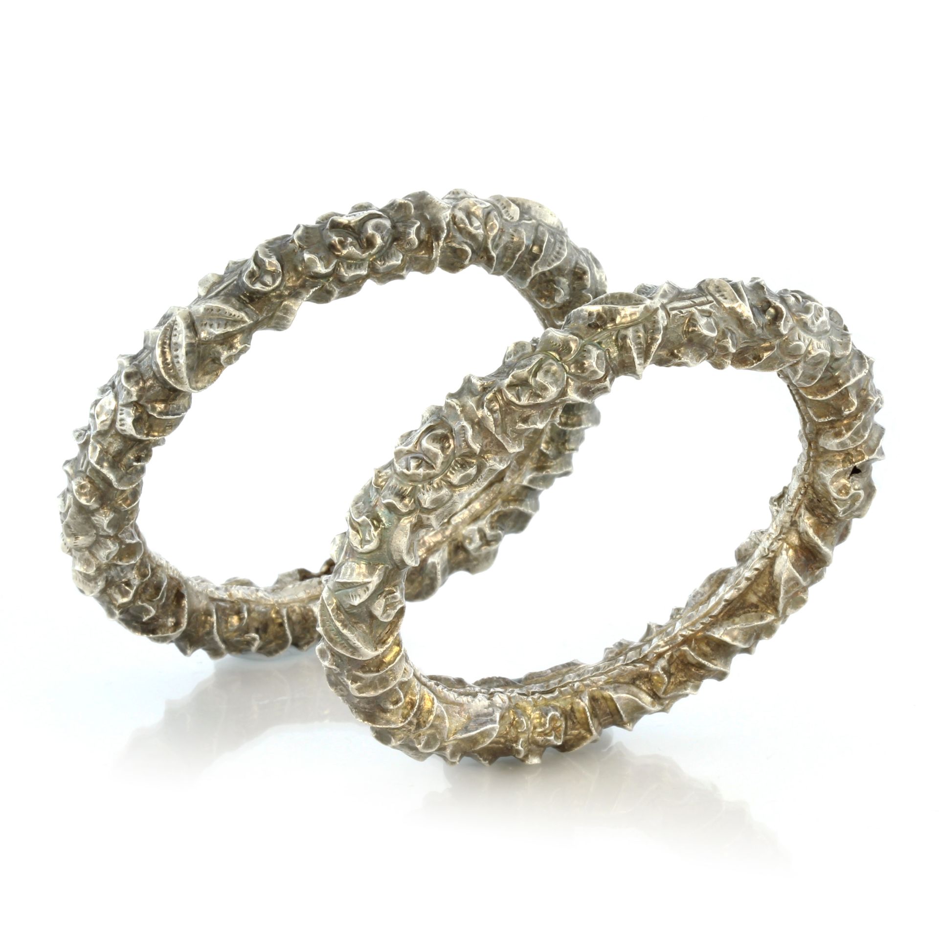 A pair of antique bangles in silver each with high relief foliate decoration. Inner diameter 6cm.