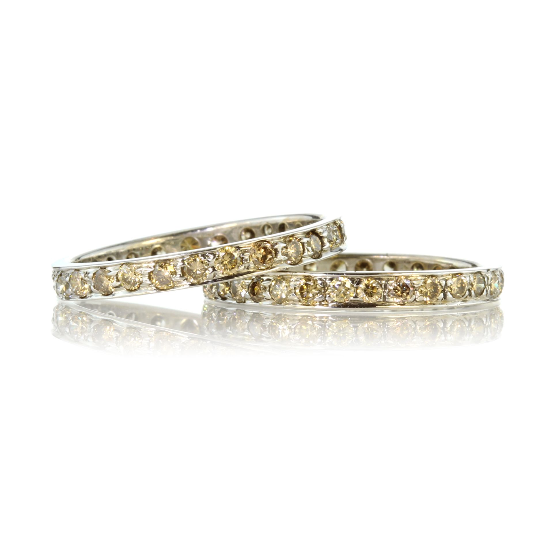 A pair of yellow diamond eternity rings in white gold each set with round cut yellow diamonds.