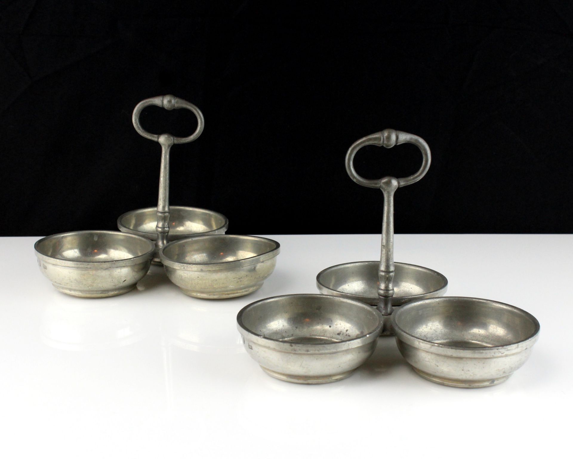 A pair of white metal condiment dishes each designed as a trio of circular dishes with a central