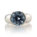 A GEM SET DRESS RING set with a large central round cut blue gemstone in a heavy, bevelled band,