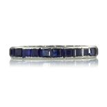 A BLUE SAPPHIRE ETERNITY RING set with a single row of square step cut blue sapphires. Ring size M /