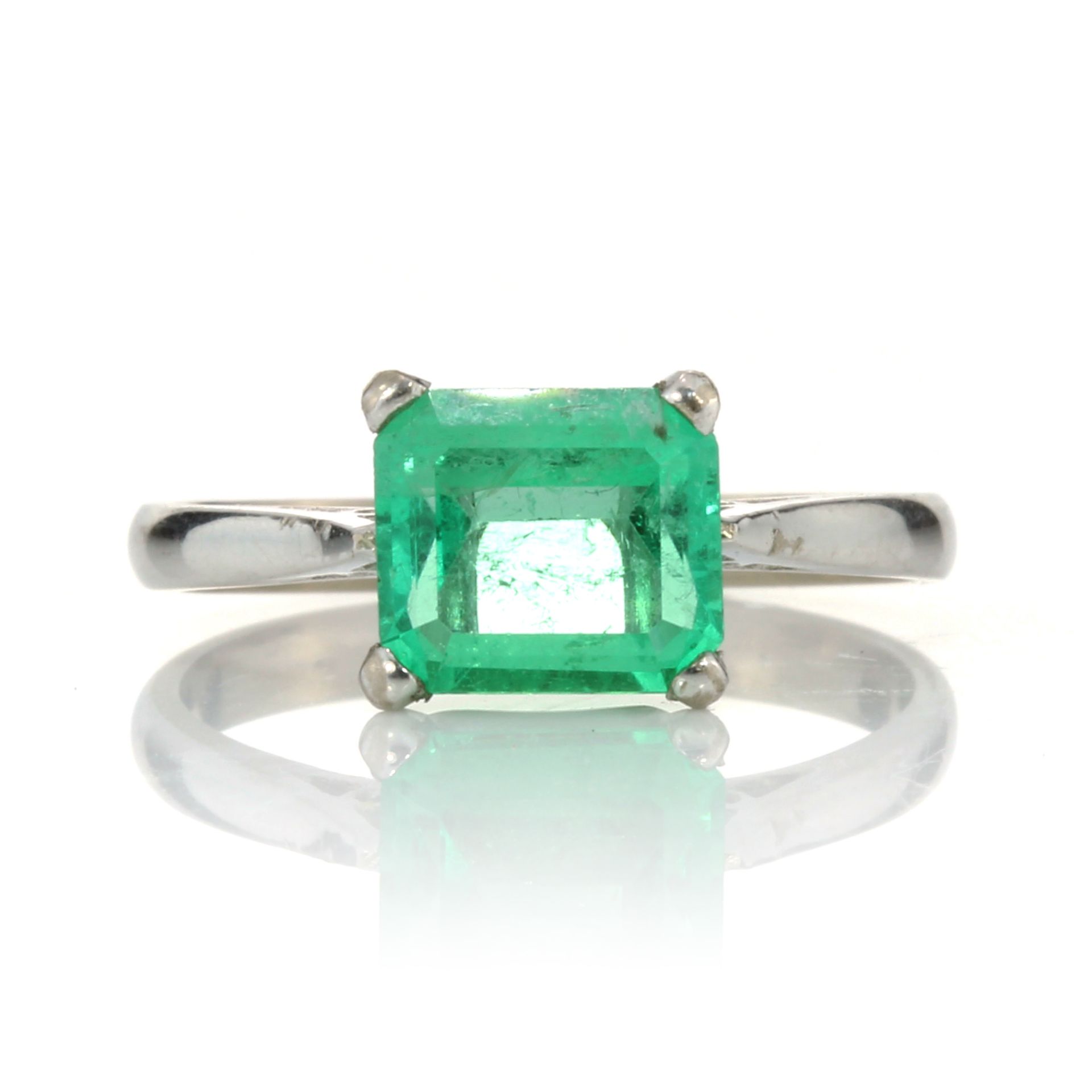 AN EMERALD DRESS RING set with a cut cornered step cut emerald of 1.86 carats to a plain tapering