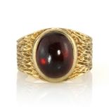 A GARNET DRESS RING, CIRCA 1970 set with a large oval cabochon garnet within a textured band, signed