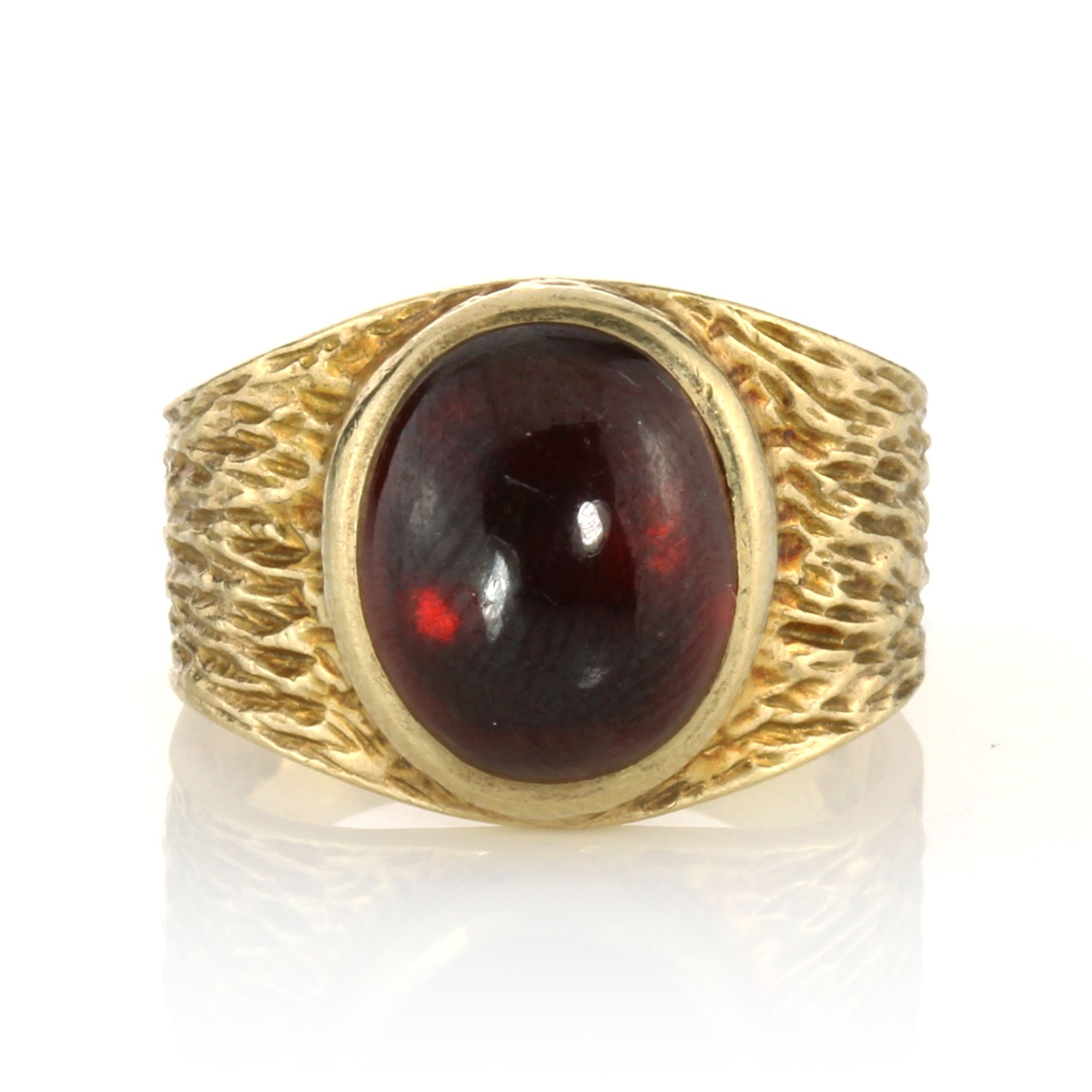 A GARNET DRESS RING, CIRCA 1970 set with a large oval cabochon garnet within a textured band, signed