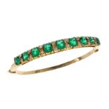 AN EMERALD AND DIAMOND BANGLE in yellow gold, set with a half hoop of graduated emerald cut emeralds