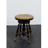 An adjustable piano stool, the circular top on turned supports with brass mounted and glass claw and