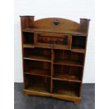 An oak Arts & Crafts bookcase with an arched ledgeback having a Ruskin style roundel plaque over a