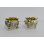A pair of Indian silver gilt salts, each with an embossed village scene, on three bun feet, (2)