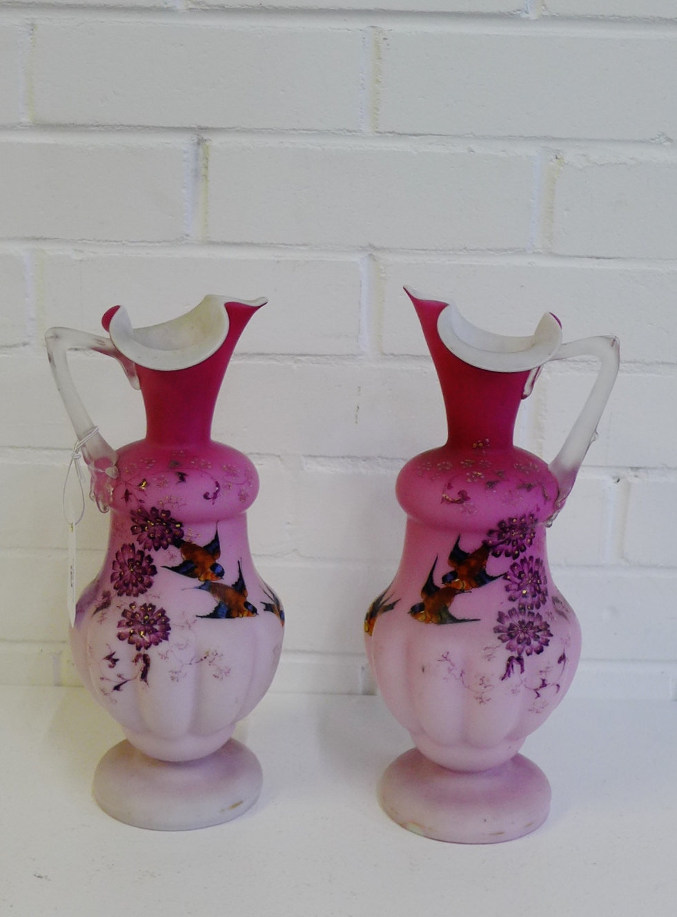 A pair of pink satin glass ewer's painted with Birds and Flowers on circular foot rims, 31cm