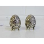 A pair of Eastern white metal elliptical shaped pepper pots, likely Indian, raised on three scroll