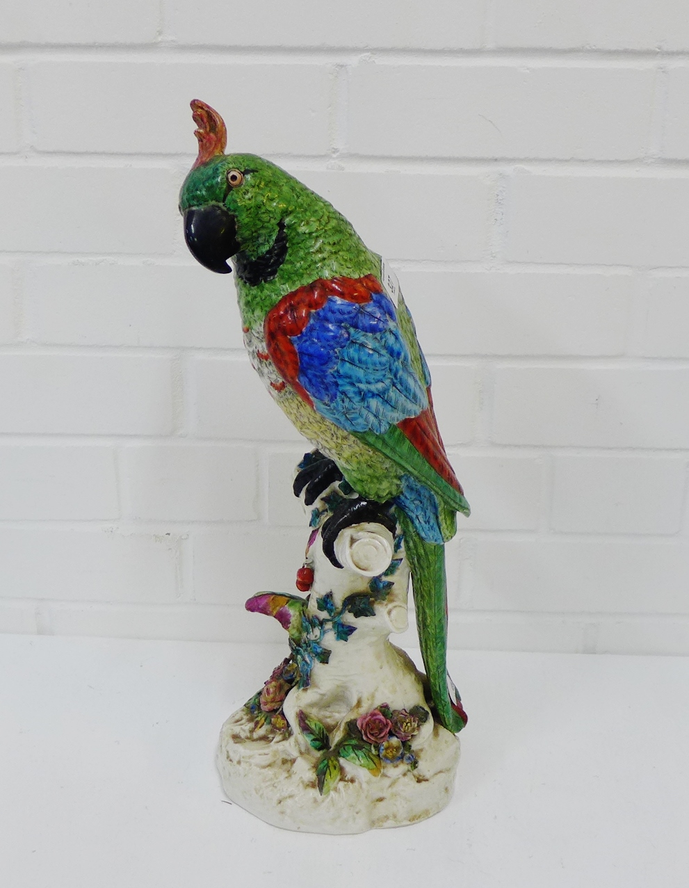 A continental porcelain modelled parrot perched upon a naturalistic floral encrusted mound, height