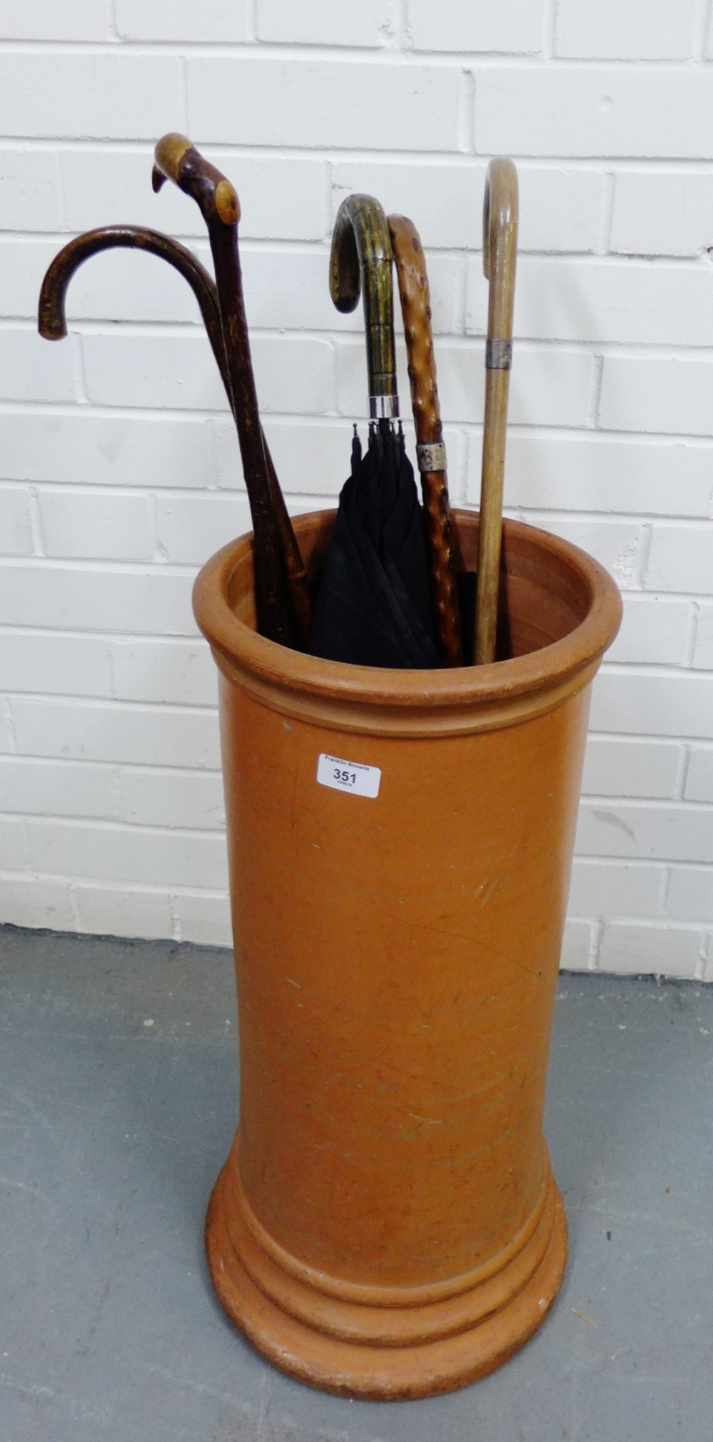 A terracotta stick stand containing a collection of vintage walking canes and an umbrella, (6)