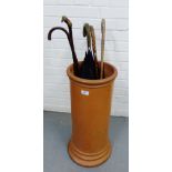 A terracotta stick stand containing a collection of vintage walking canes and an umbrella, (6)