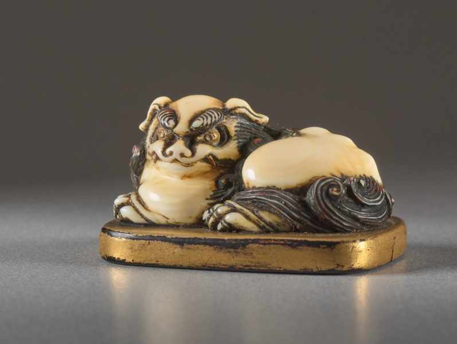 AN IVORY AND LACQUER NETSUKE OF A RECUMBENT SHISHI ON MAT Ivory netsuke with gold lacquer. Japan, - Image 2 of 5