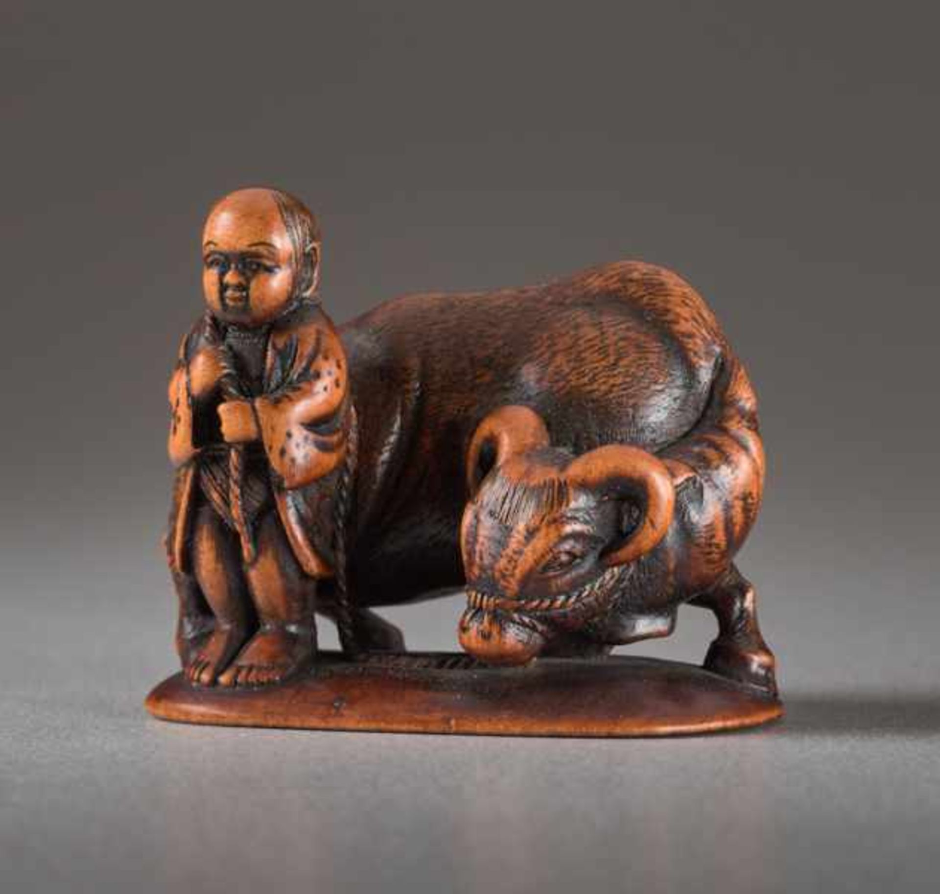 A WOOD NETSUKE BY MINKOKU OF A BOY AND OX Wood netsuke. Japan, 19th centuryA brawny ox with curved