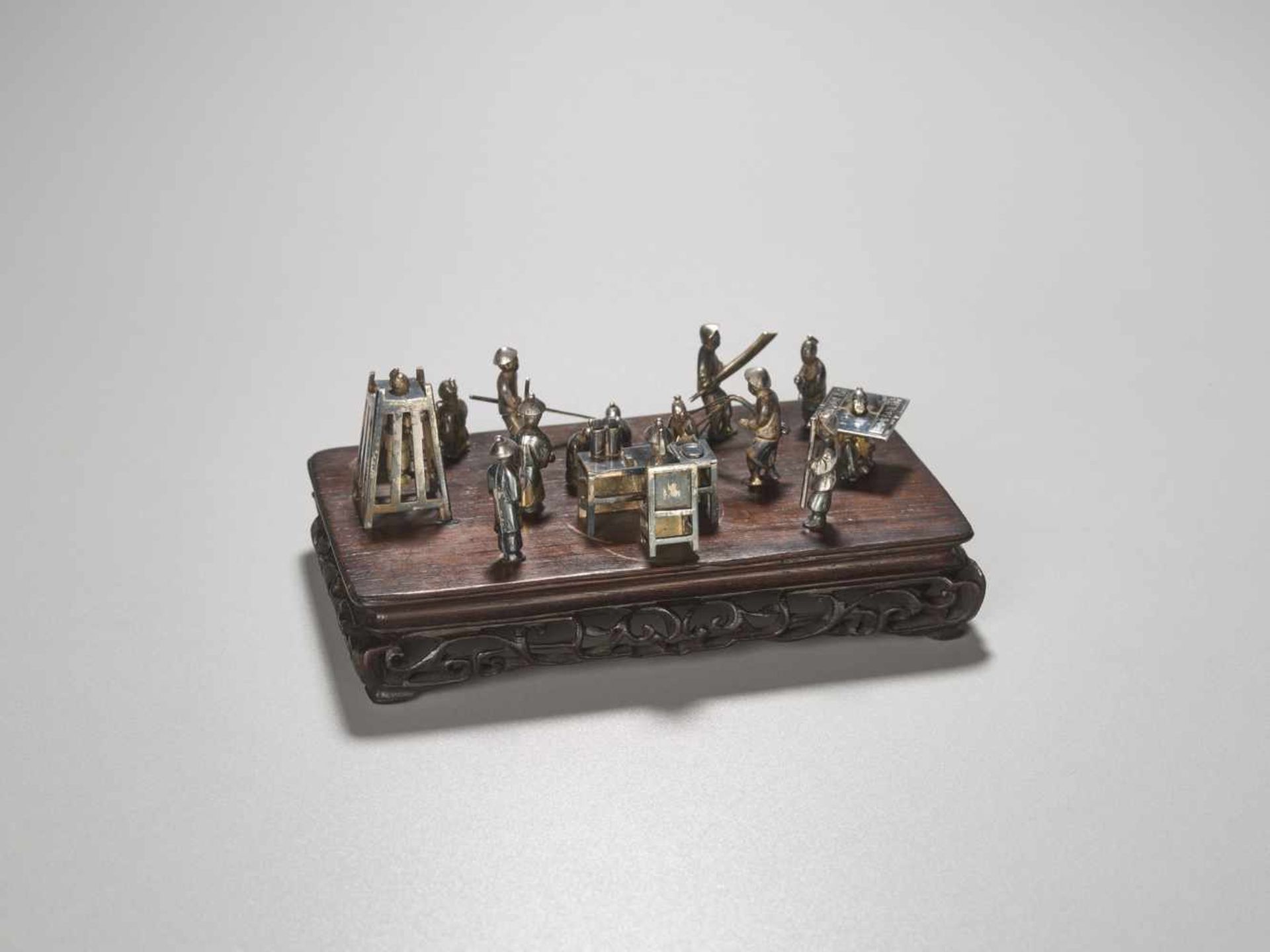 A QING DYNASTY SILVER MINIATURE GROUP ‘MAGISTRATE HOLDING COURT’ Silver and metal, wooden base