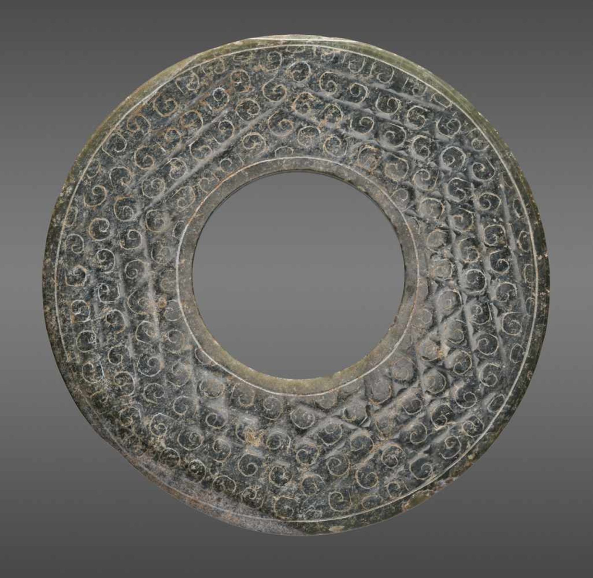 A SHINY GREEN DISC WITH A DELICATE PATTERN OF INCISED SCROLLS Jade. China, Han Dynasty, 2nd