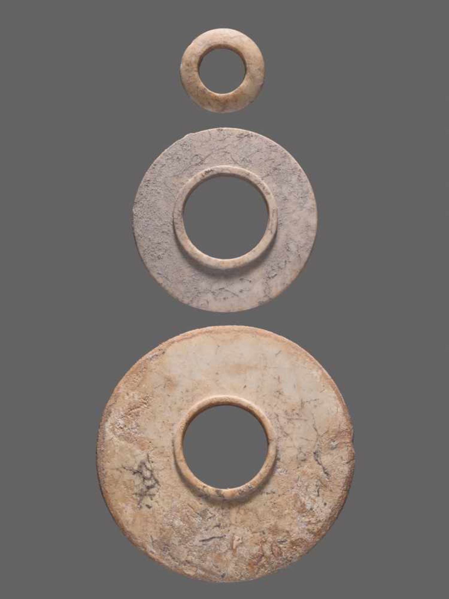 A GROUP OF TWO HEAVILY ALTERED SHANG PERIOD JADE DISCS AND A RING, ALL WITH A BEAUTIFUL