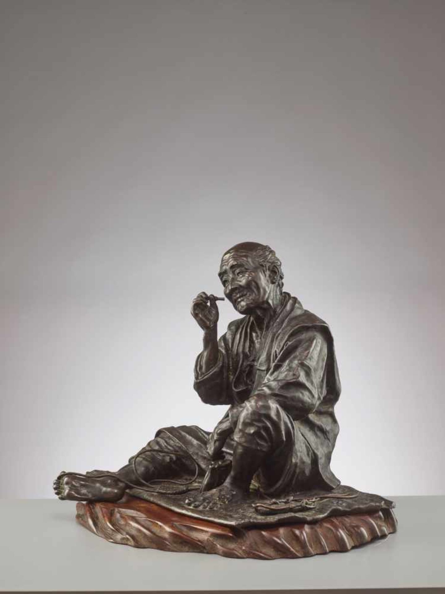 A FINE AND LARGE JAPANESE BRONZE OF A ZORI SANDAL MAKER TAKING A SMOKING BREAK BY TAKAHASHI RYOUN