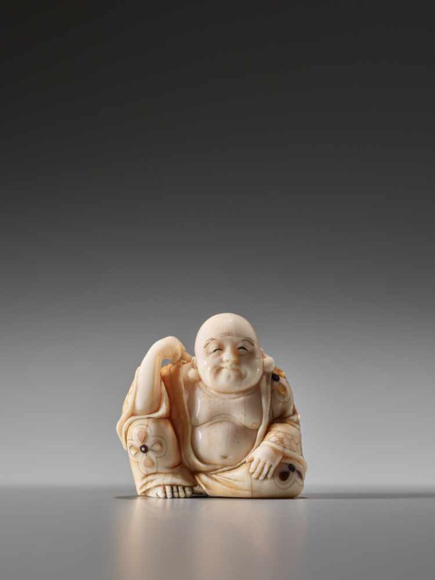 A TOKYO SCHOOL INLAID SPERM WHALE TOOTH NETSUKE OF HOTEI SCRATCHING HIS BACK BY GYOKUZANSperm