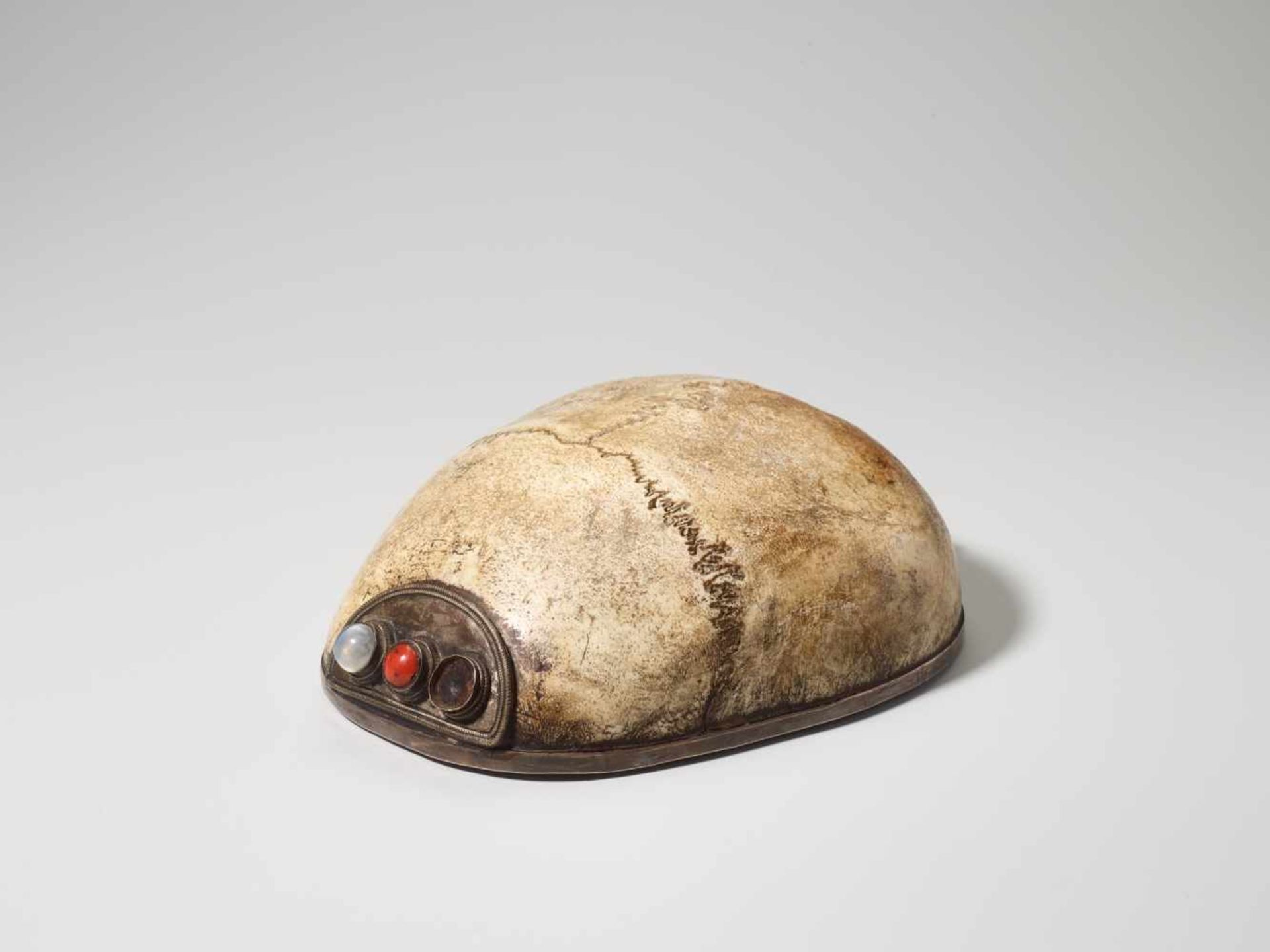 A LINED AND CABOCHON INSET RITUAL KAPALA SKULL CAP, 19th CENTURY Bone, silver-plate copper, coral