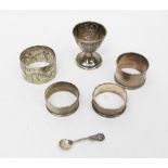 Three silver napkin rings and a silver egg cup, a small sterling salt spoon with shell bowl,