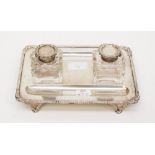 An Edward VII silver ink stand, plain rectangular body raised on scroll feet,