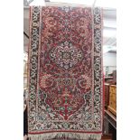 A 20th Century hand knotted woollen runner rug, with symmetrical floral decoration on a red ground,