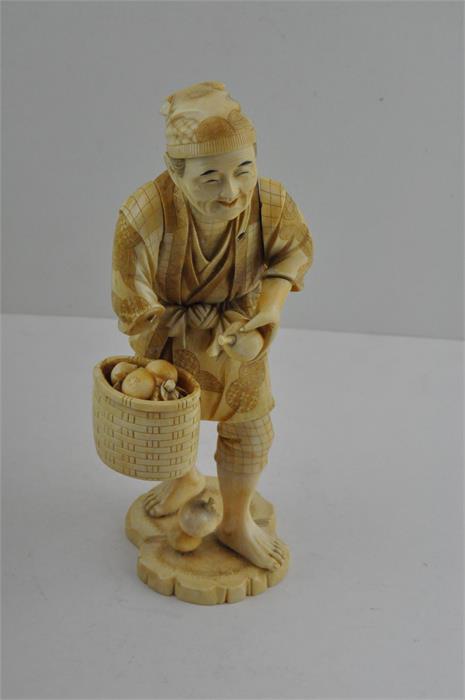 A Japanese Meiji period carved ivory okimono, of a fruit seller on stand, signed, height 25 cm.