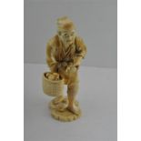 A Japanese Meiji period carved ivory okimono, of a fruit seller on stand, signed, height 25 cm.