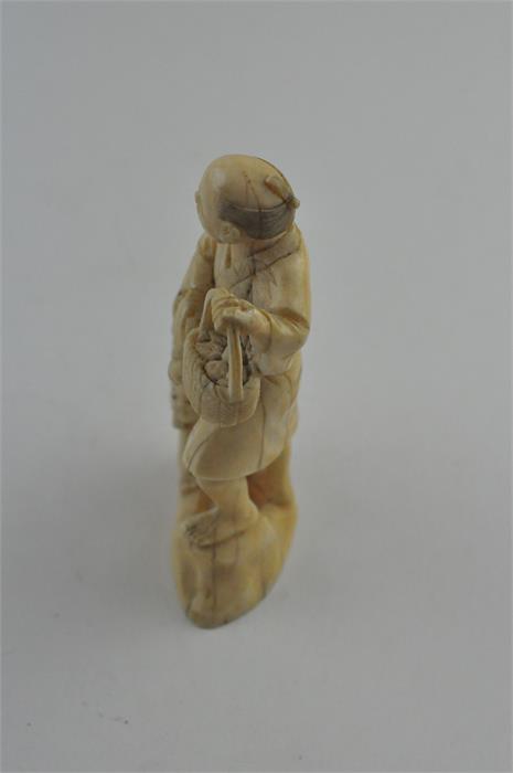 A Japanese Meiji period carved ivory okimono, of a man carrying a basket of fruit with children to - Image 2 of 6
